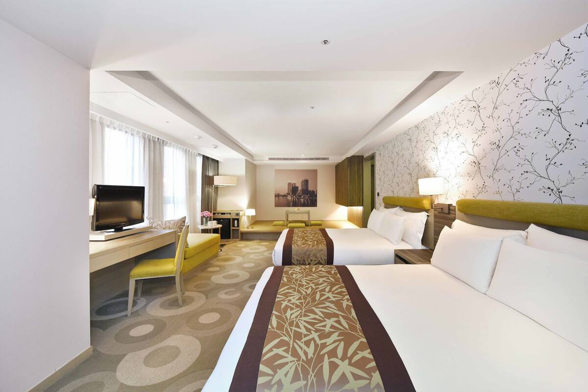 Een hotelkamer met twee bedden, een bureau met een televisie, en een stadszicht door het raam.