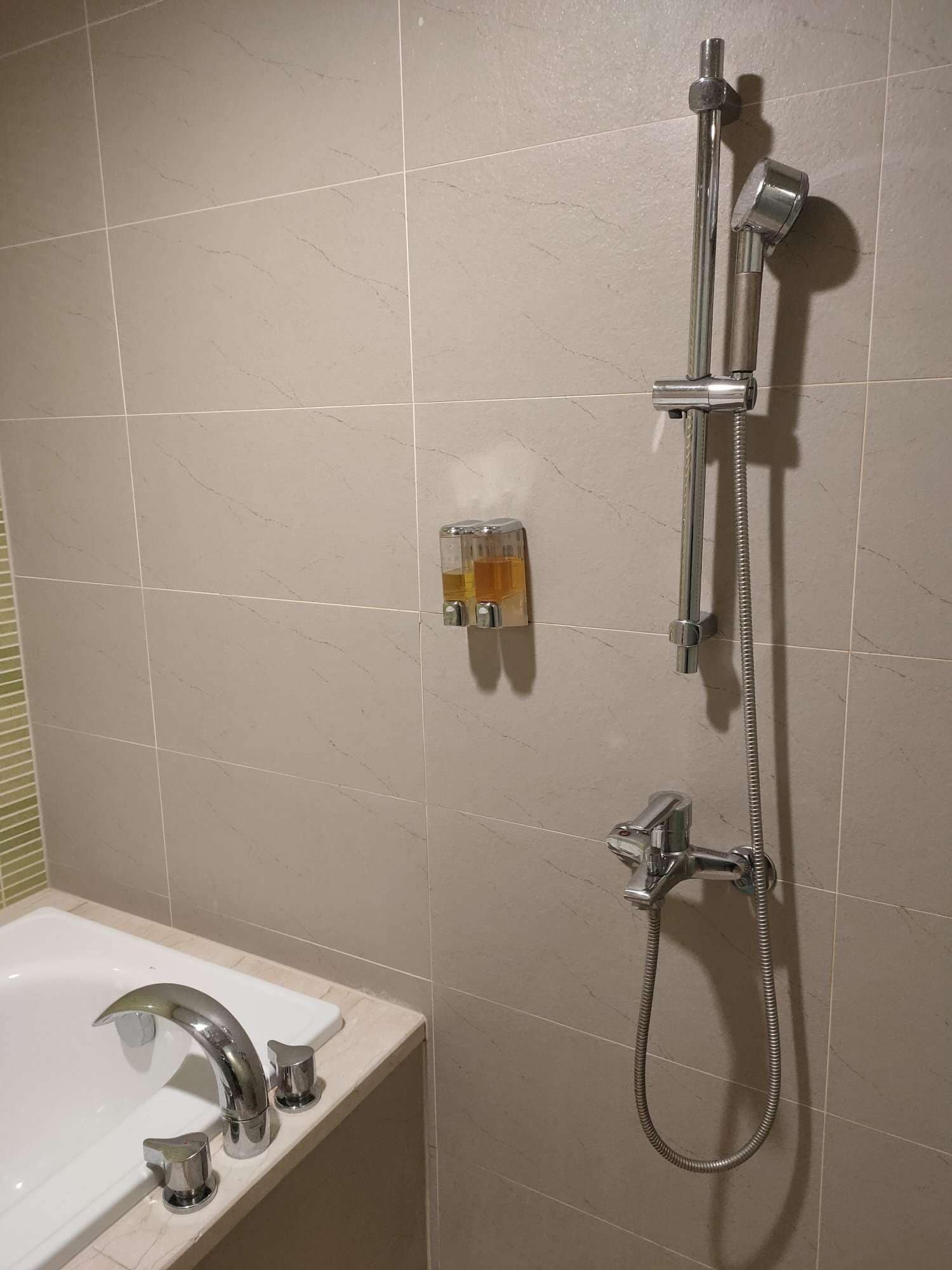 A bathroom with a bathtub, a shower with a handheld showerhead, and a soap dispenser on the wall.