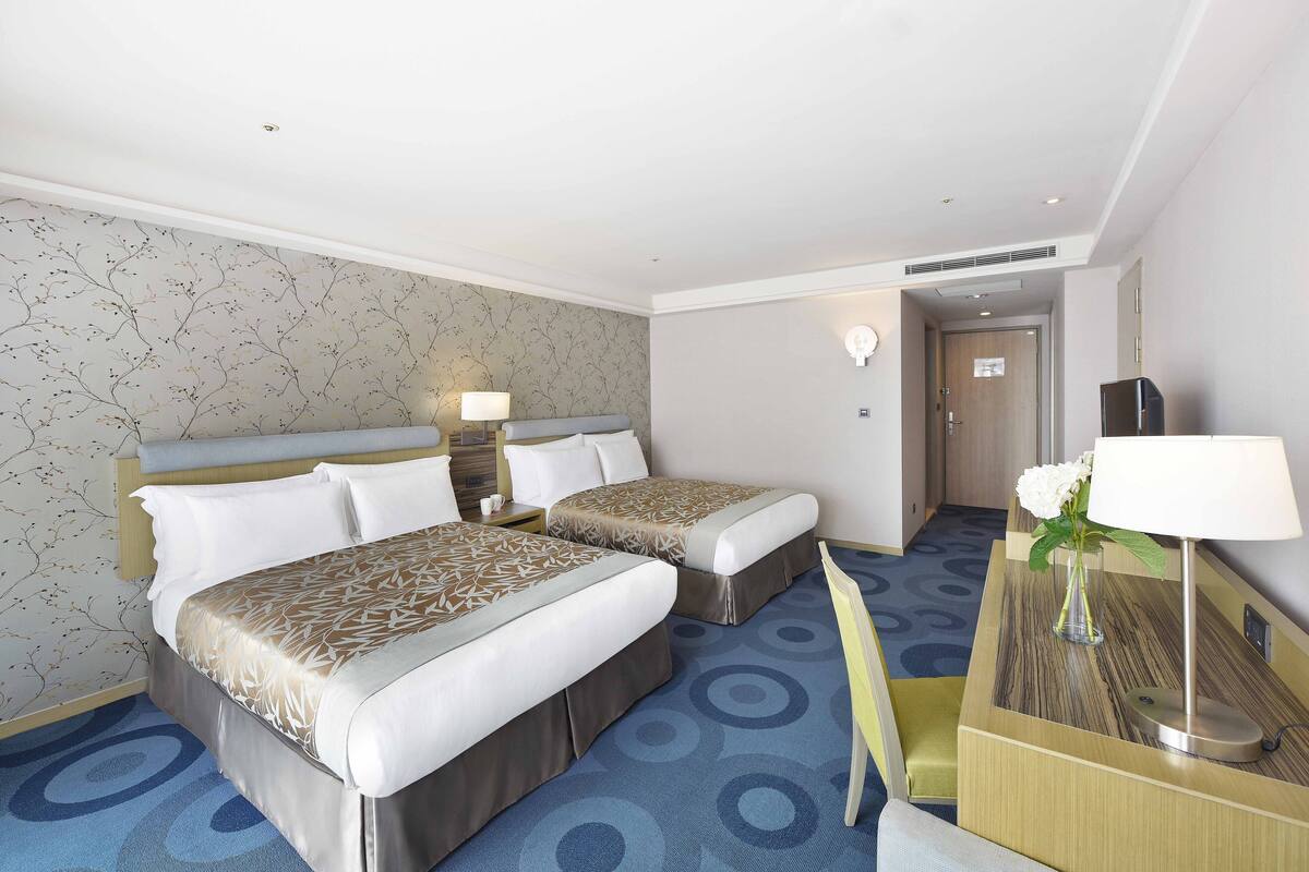 Een hotelkamer met twee bedden, een bureau, een lamp en een vaas met bloemen.