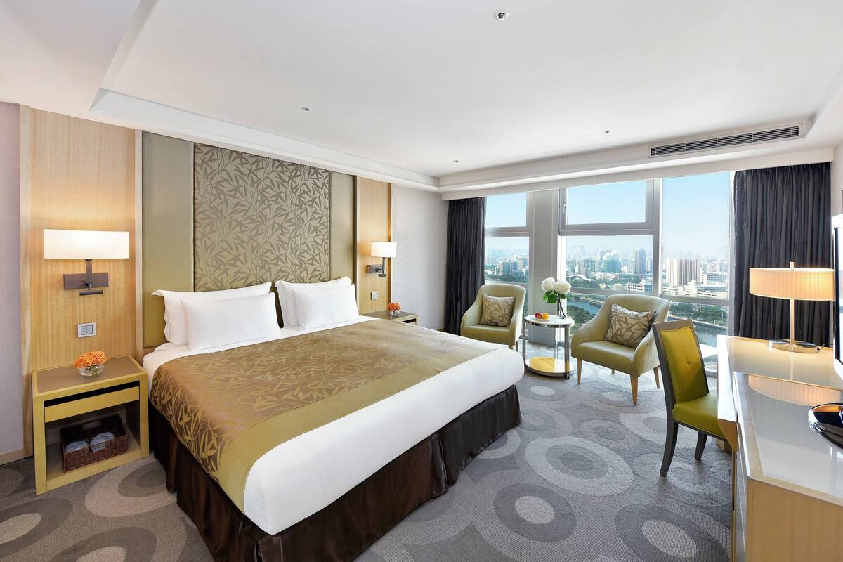 Een hotelkamer met een groot bed, twee stoelen, een bureau en uitzicht op de stad.
