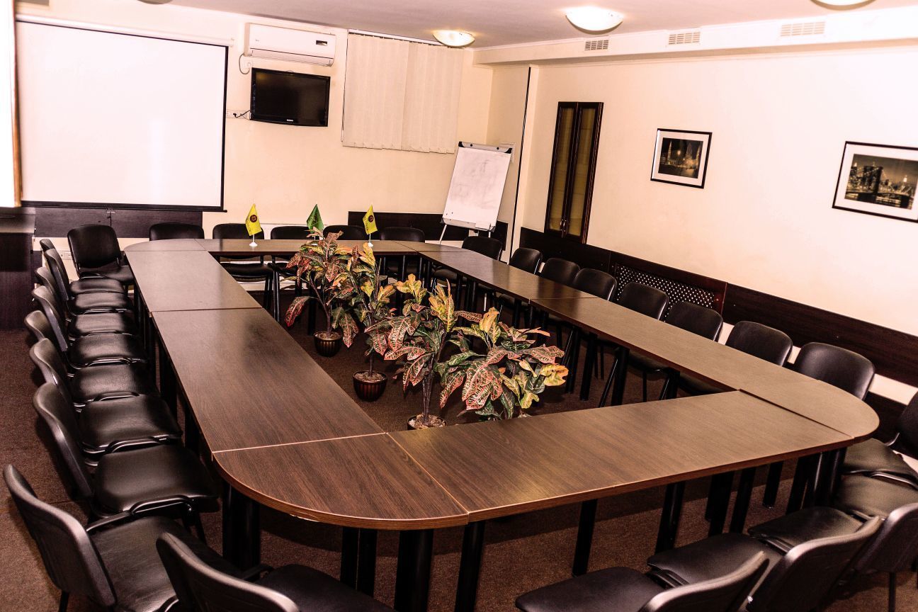 Een vergaderruimte met een lange tafel, zwarte stoelen, een whiteboard en potplanten.