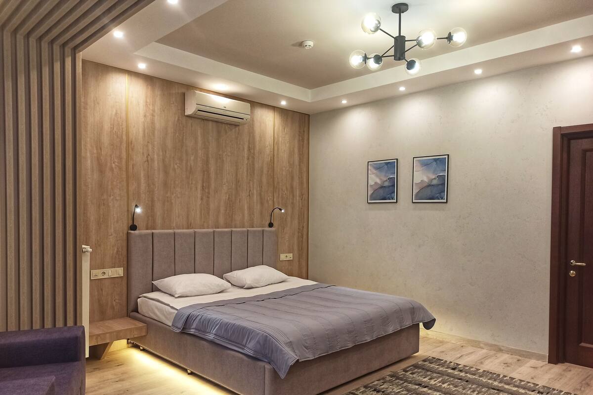 Un dormitorio moderno con una cama, aire acondicionado empotrado, luces en el techo y una alfombra estampada.