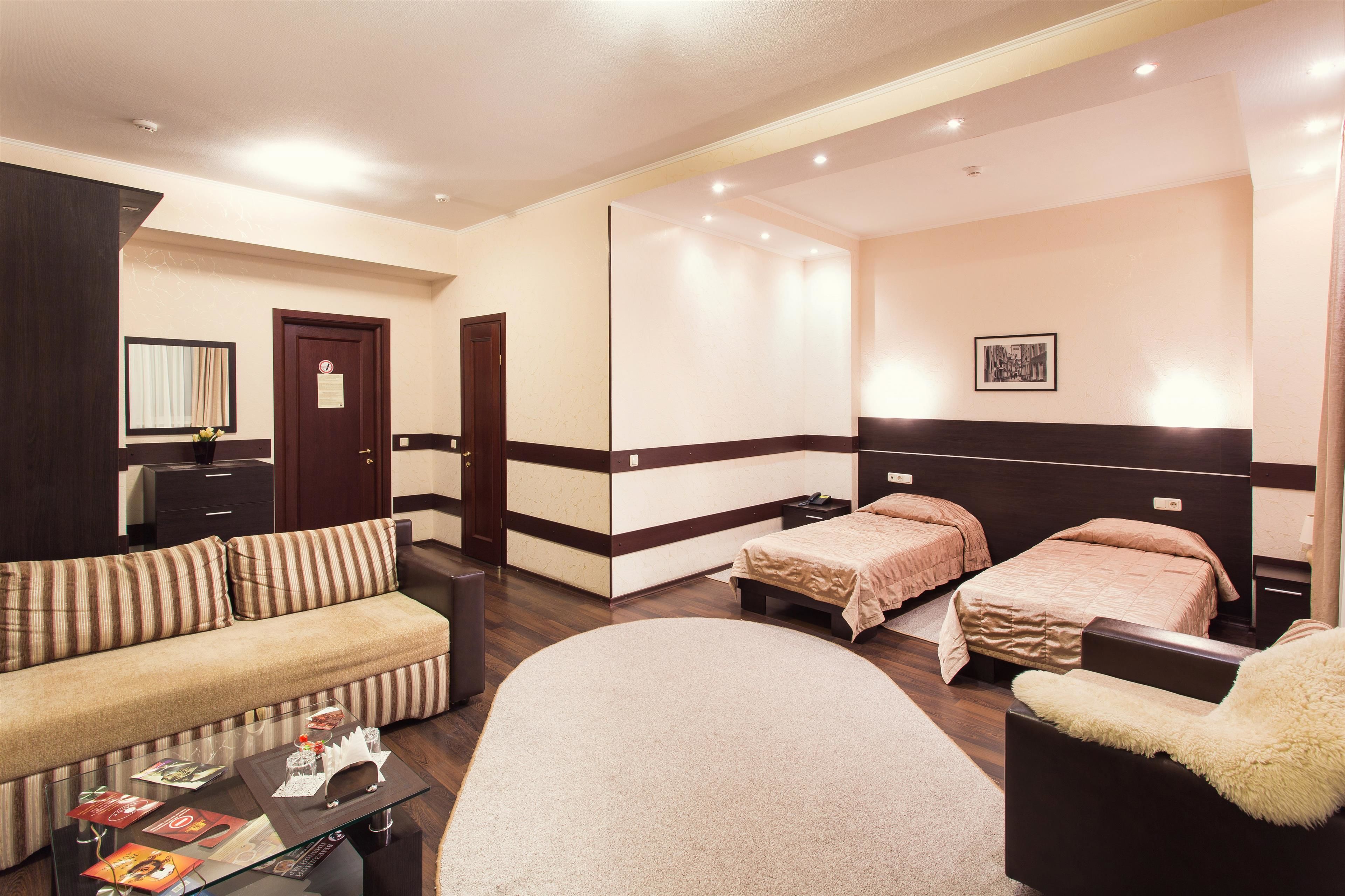 Ein Hotelzimmer mit einer Couch, zwei Einzelbetten, einem Sessel, einem kleinen Tisch und einem Spiegel.