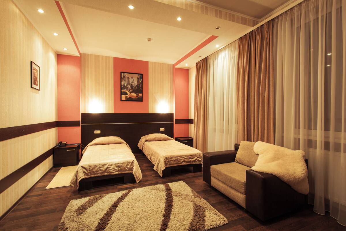 Habitación de hotel con dos camas, un sofá, un ventanal con cortinas y un cuadro en la pared.