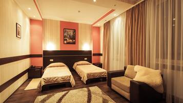 A hotel room with two beds, a sofa, a large window with curtains, and a painting on the wall.