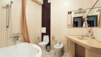 A modern bathroom with a bathtub, toilet, bidet, and a large mirror.