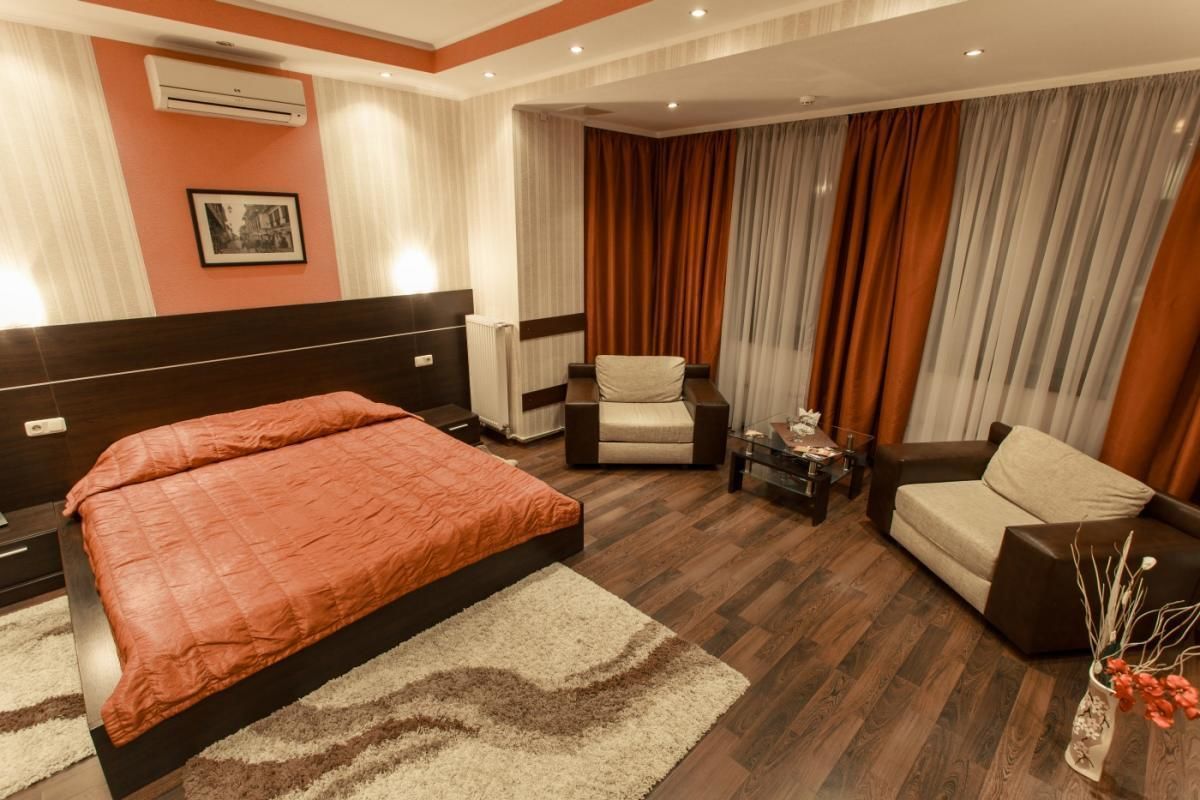 A hotel room with a large bed, a chair, a sofa, a small table, and a vase with flowers.