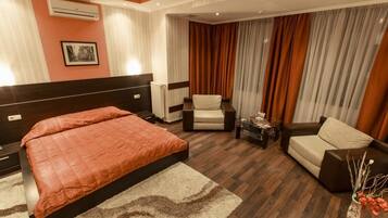 A hotel room with a large bed, a chair, a sofa, a small table, and a vase with flowers.