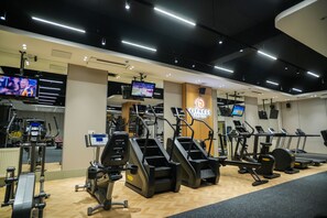 A gym with multiple treadmills, ellipticals, and a television screen displaying a sports event. - Ramada by Wyndham Ulaanbaatar Citycenter (Ulaanbaatar)