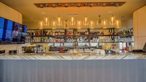 Una zona de bar con mostrador de mármol, lámparas colgantes y estantes llenos de botellas de licores.