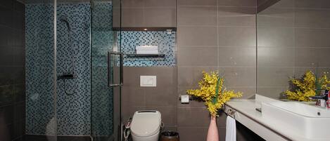 A modern bathroom with a glass shower enclosure, a toilet, a sink with a mirror, and a vase with yellow flowers.