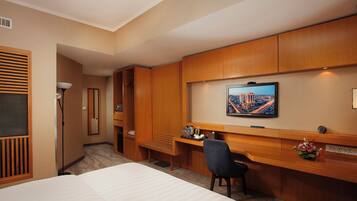 A hotel room with a bed, a desk with a chair, a television, and a view of a cityscape.