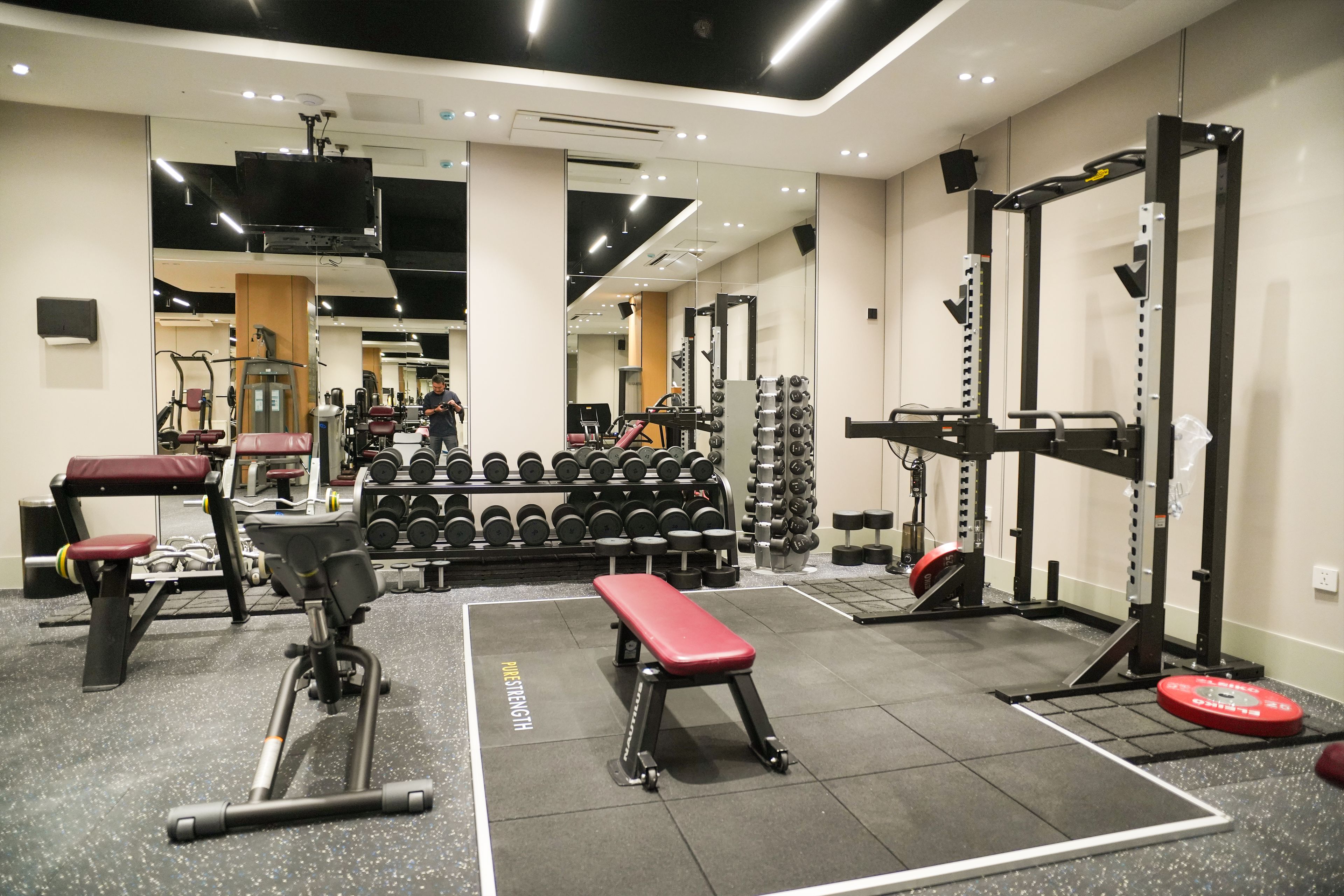 Un gimnasio con equipo de levantamiento de pesas, bancos y un espejo.