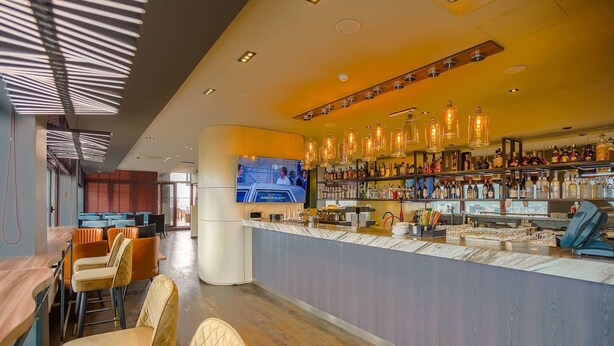 Un área de bar moderna con una barra larga, taburetes y una pantalla de televisión.