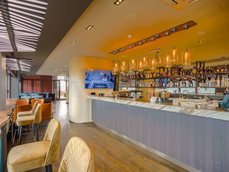 Un área de bar moderna con una barra larga, taburetes y una pantalla de televisión.