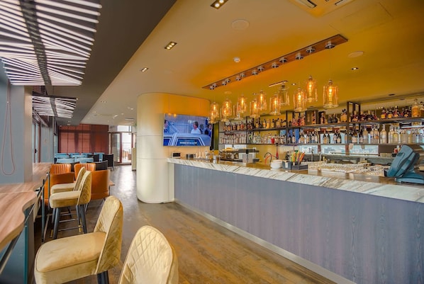 A modern bar area with a long counter, bar stools, and a television screen.