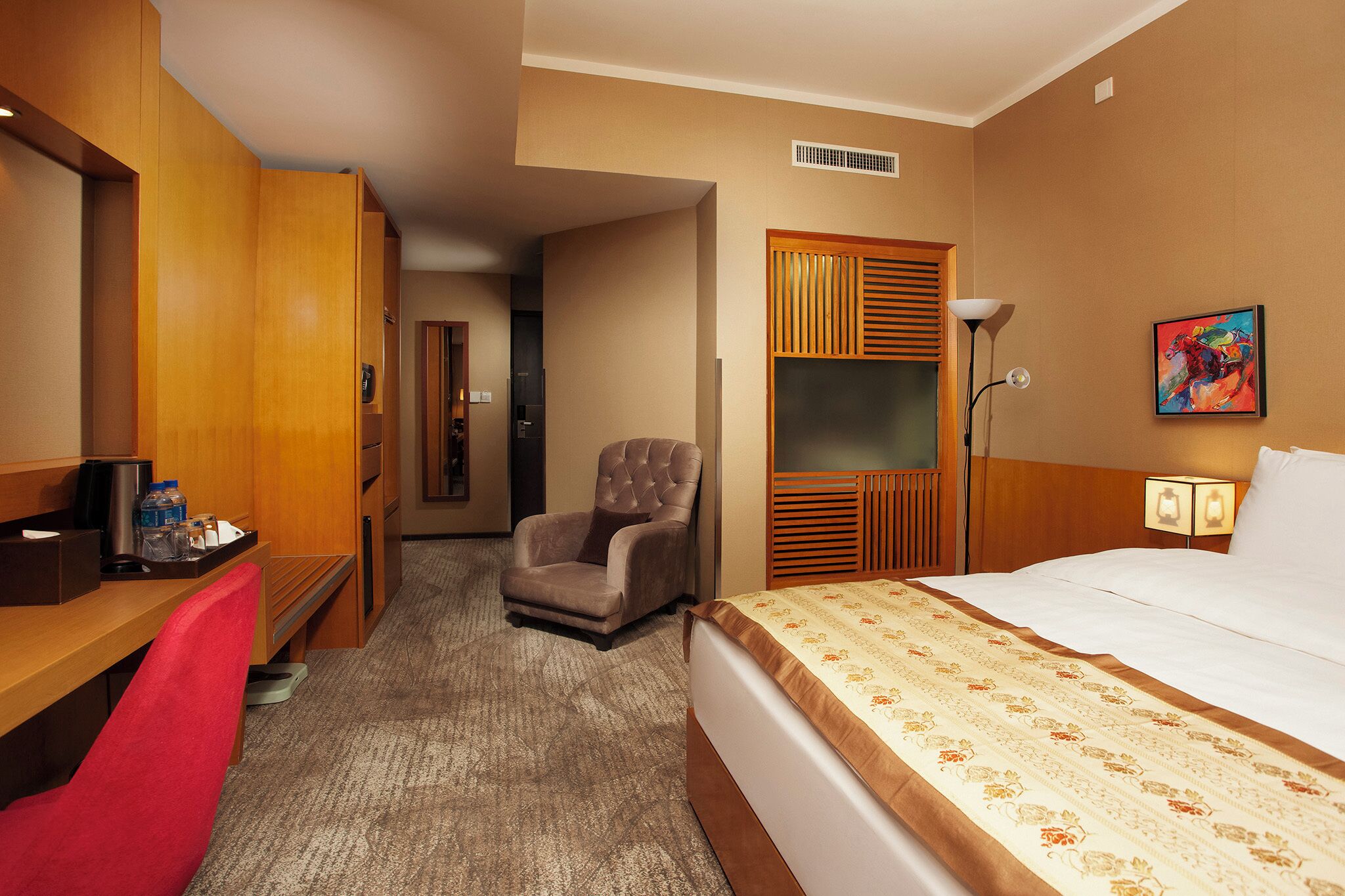 Habitación de hotel con cama, escritorio, silla, televisión y un cuadro en la pared.