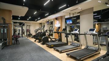 A modern gym with various cardio machines, weightlifting equipment, and a digital display.