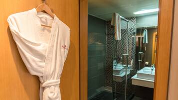 A bathroom with a glass shower enclosure, a white sink, and a wooden door with a hanging bathrobe.