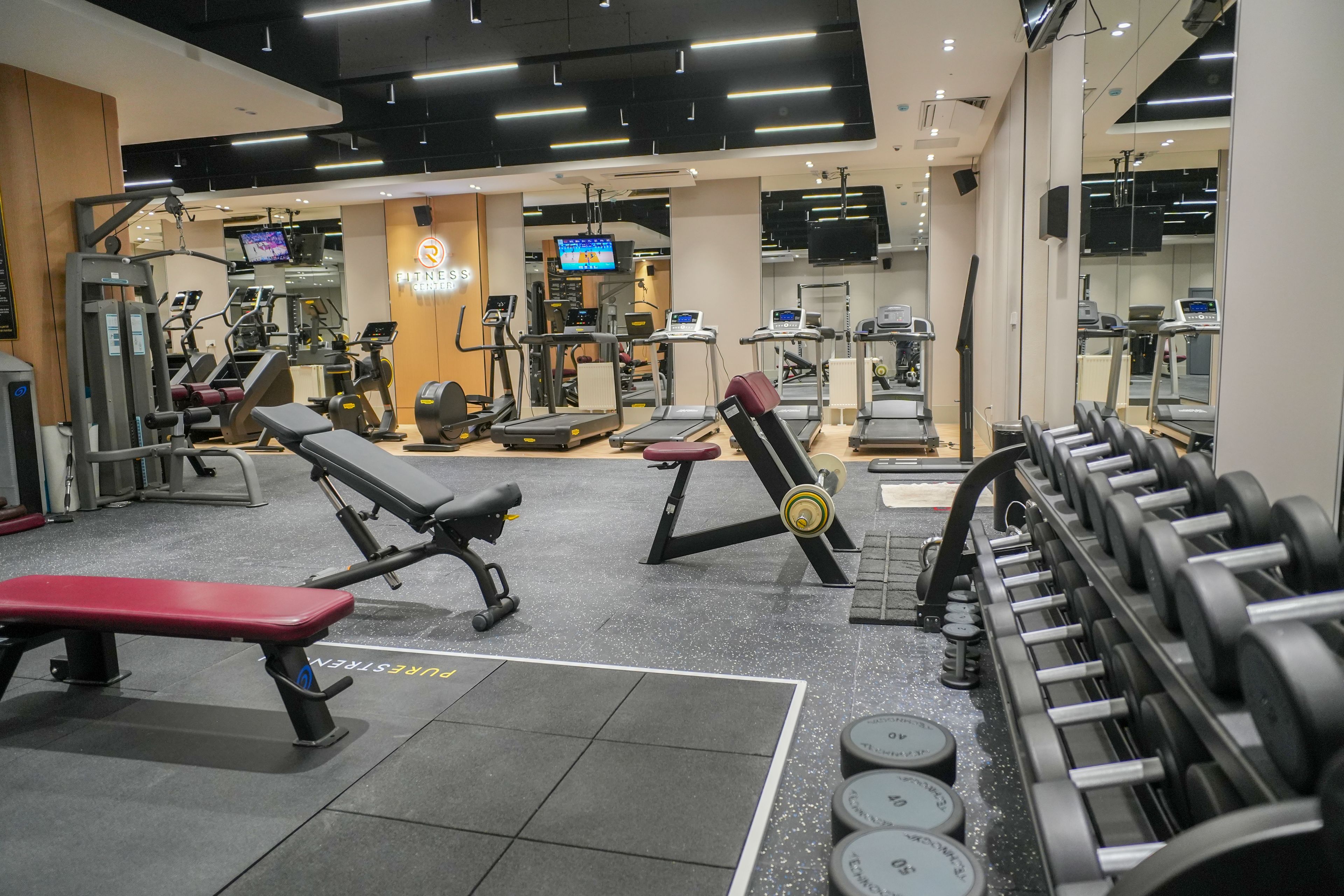 A gym with various exercise equipment, including treadmills, weight machines, and dumbbells.