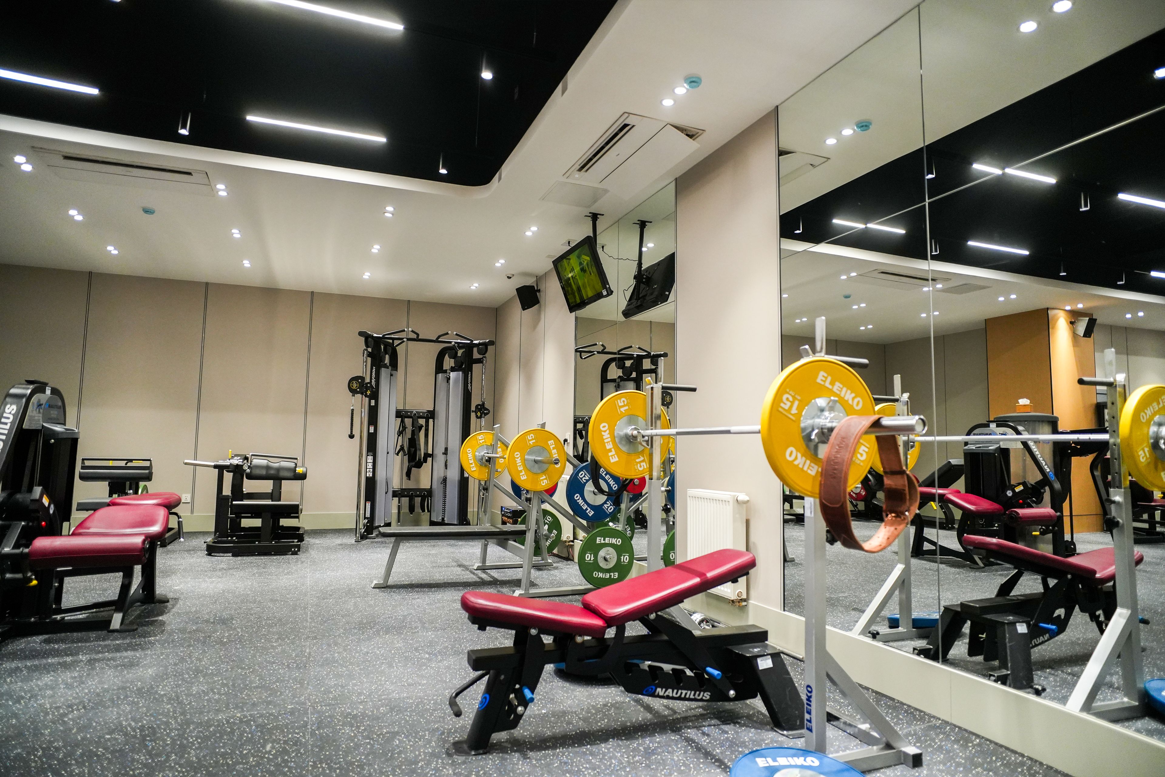 A gym with weightlifting equipment, benches, and a mirrored wall.