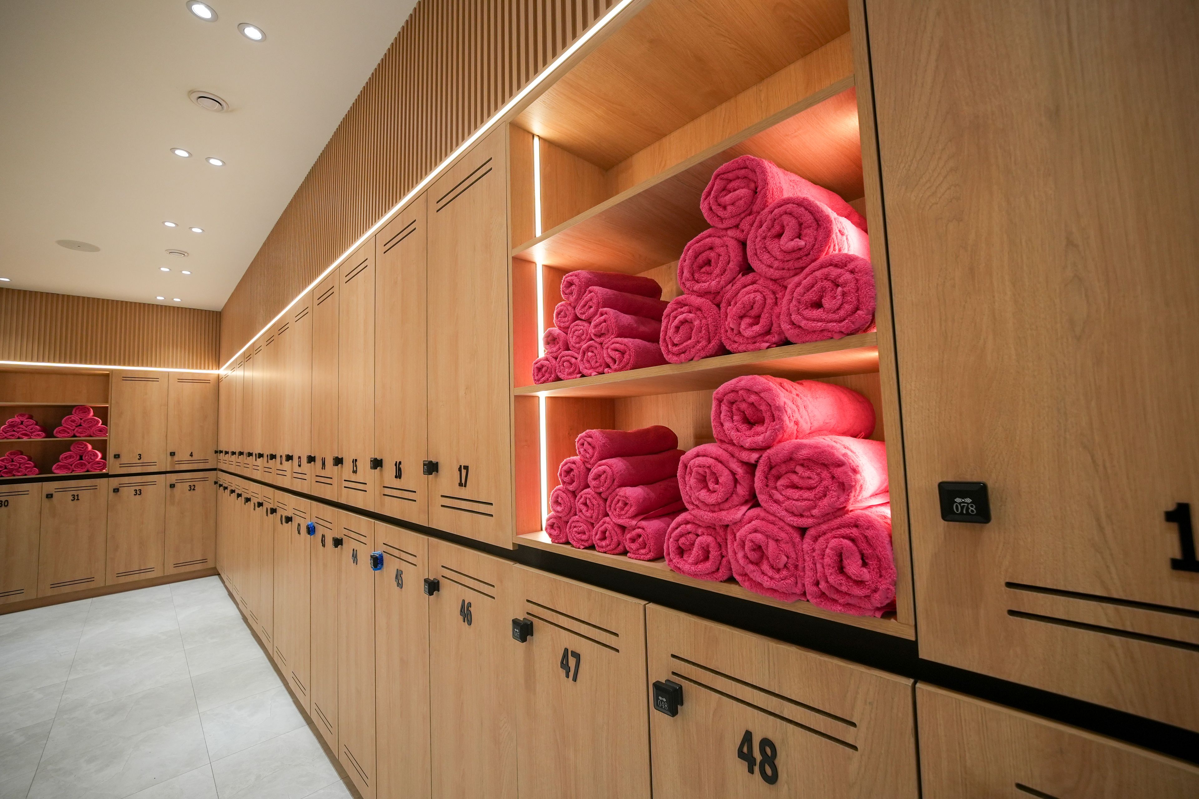 Habitación de hotel con taquillas de madera, numeradas del 1 al 48, y estantes con toallas enrolladas ordenadamente.