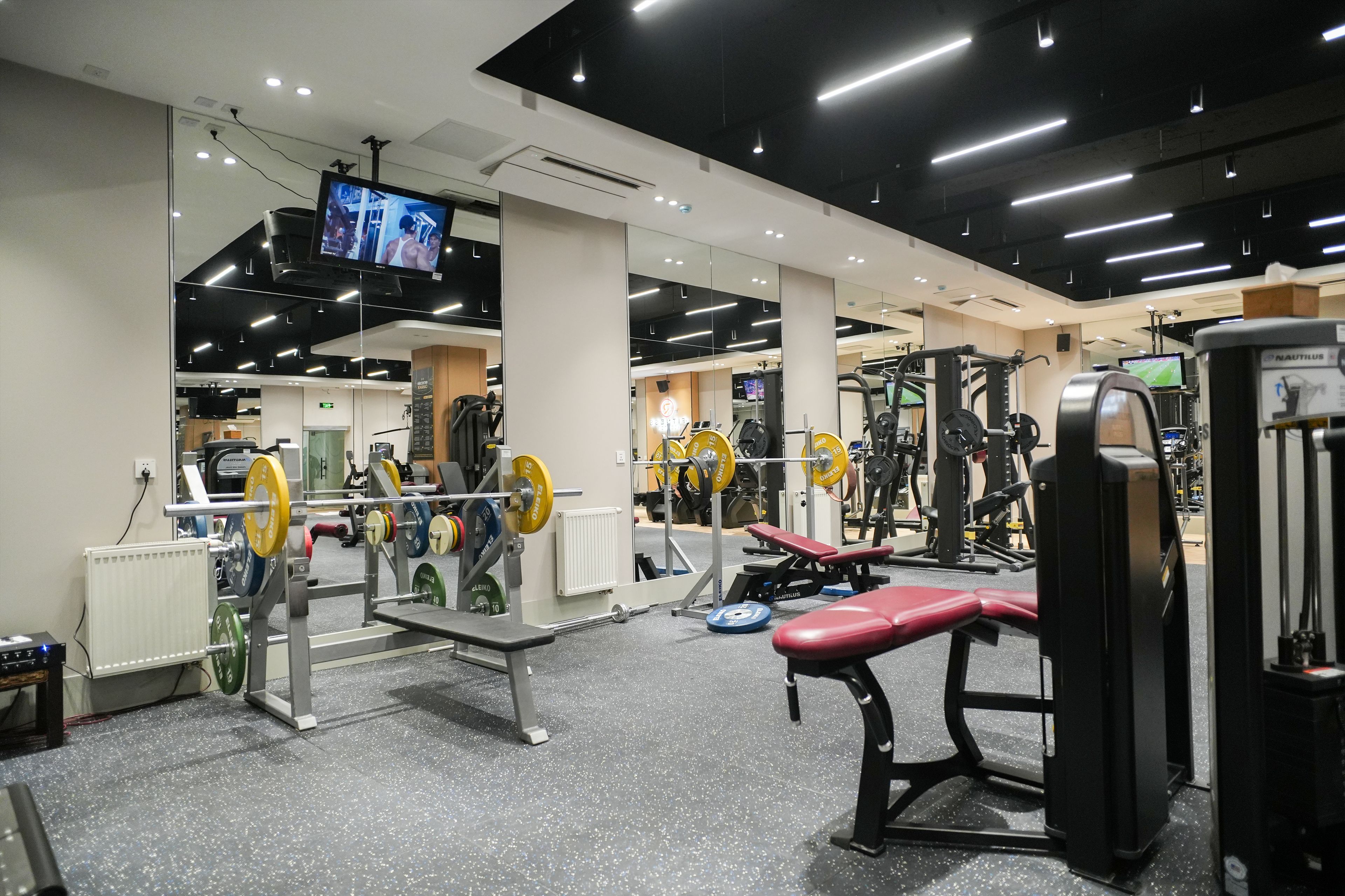 A gym with weightlifting equipment, exercise machines, and a television screen.