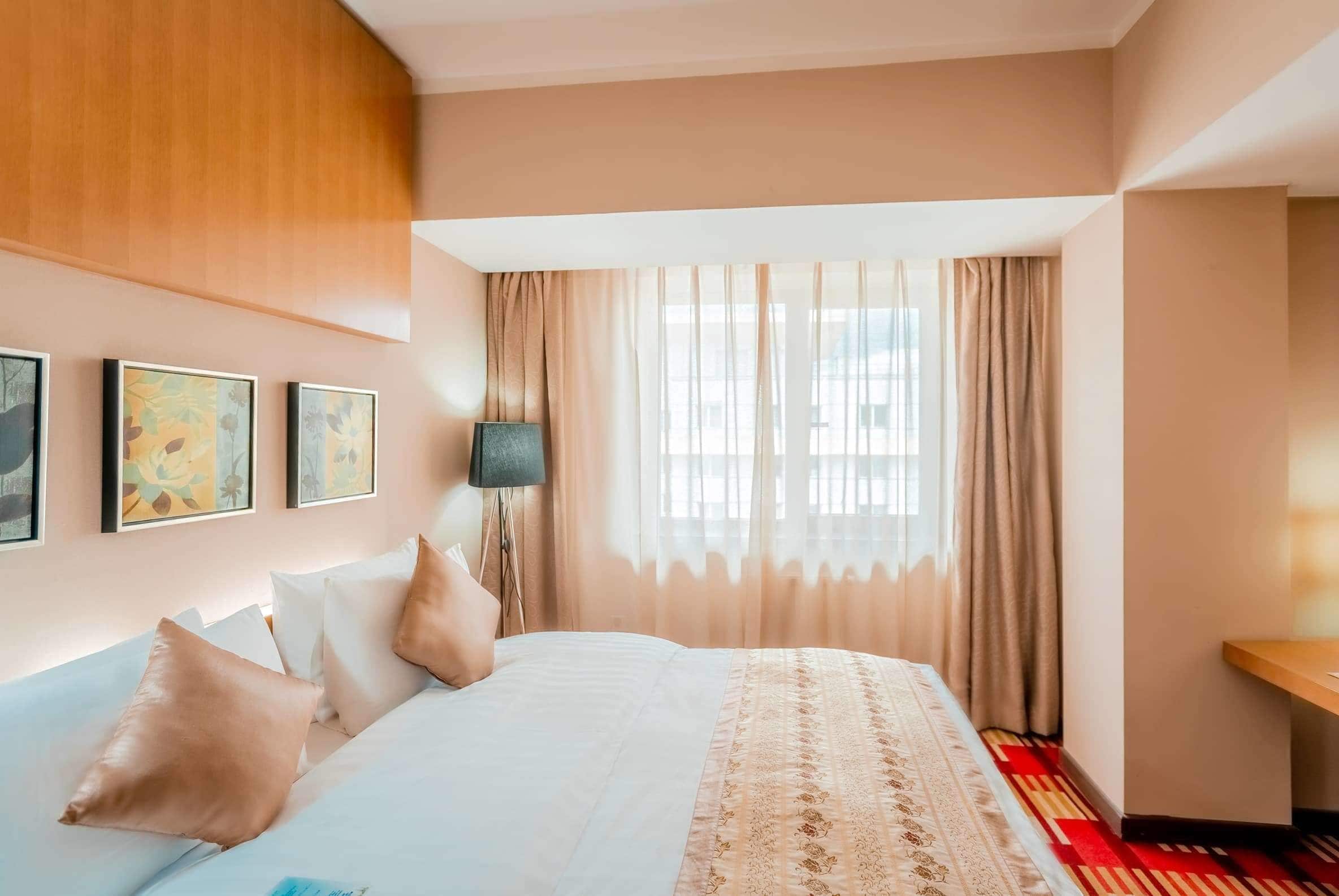 A hotel room with a large bed, a bedside table, a lamp, and a window with curtains.
