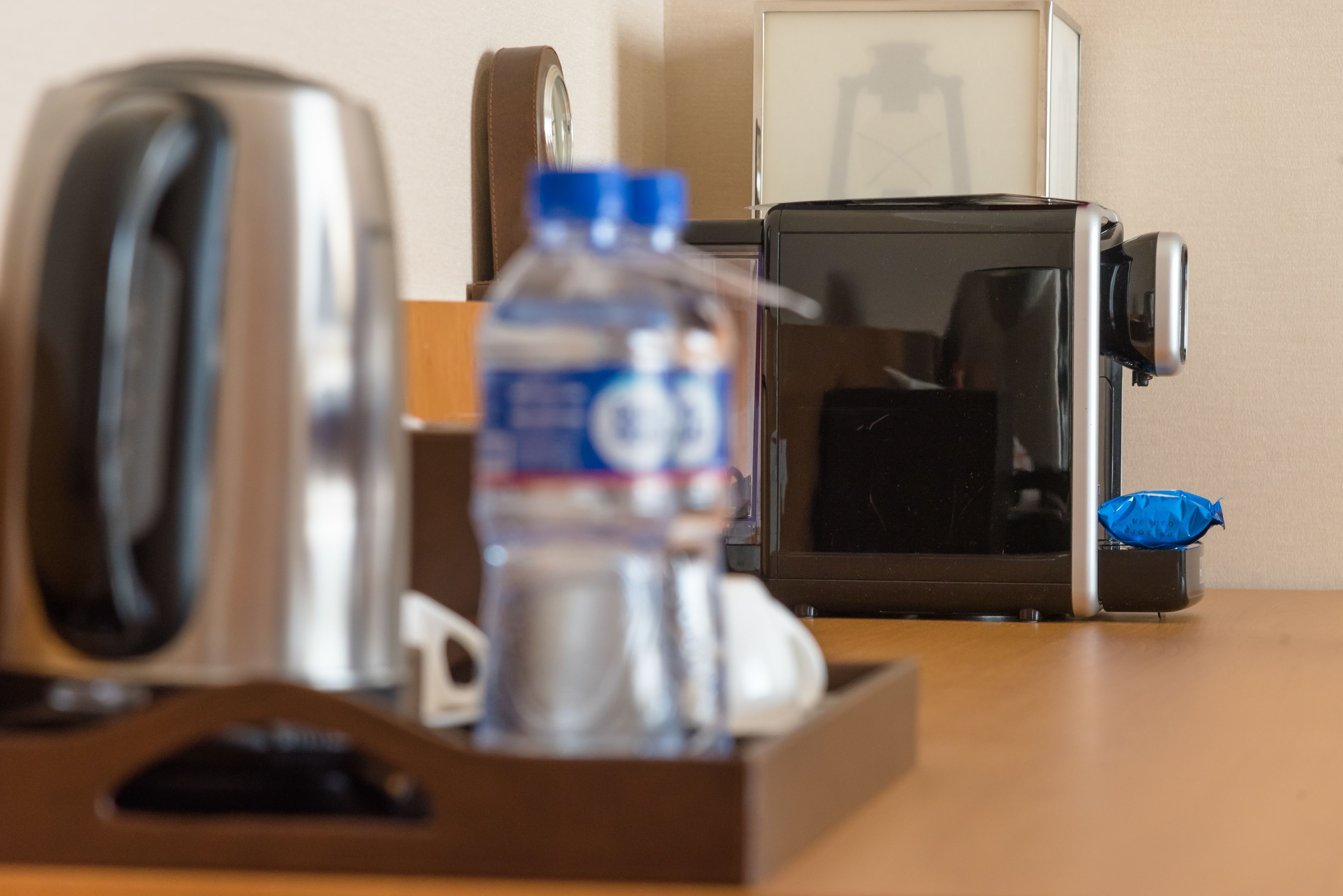 A coffee maker, a water bottle, and a microwave on a wooden table.