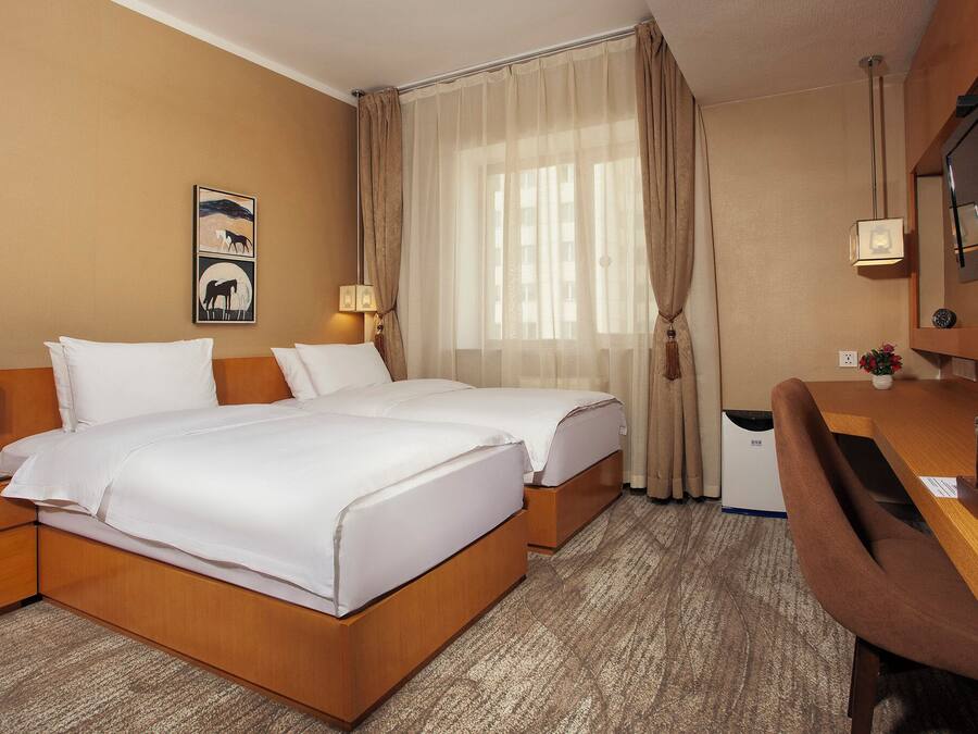 Habitación de hotel con dos camas, un escritorio, una silla, un televisor y una ventana con cortinas.