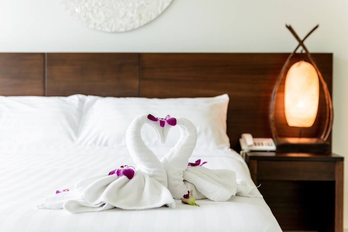 A neatly made bed with white linens and two swan-shaped towels with purple flowers.