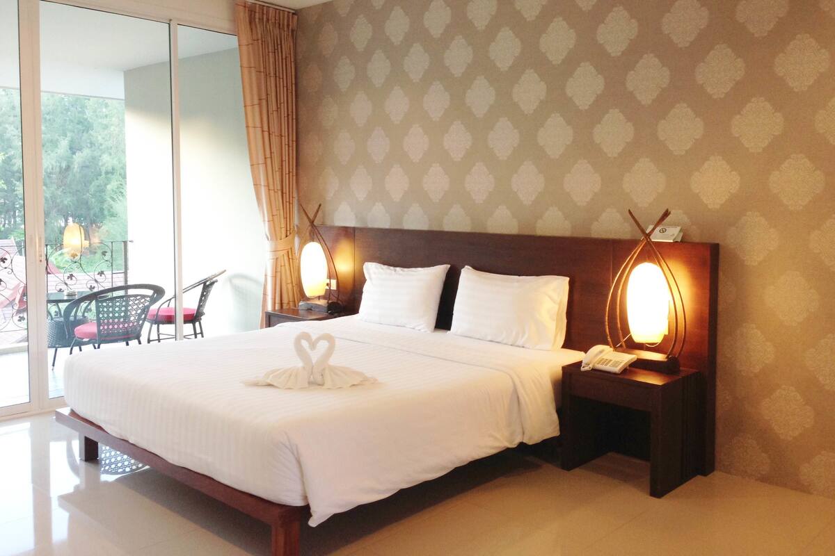 A hotel room with a large bed, two bedside lamps, a telephone, and a view of the outdoors through a glass door.