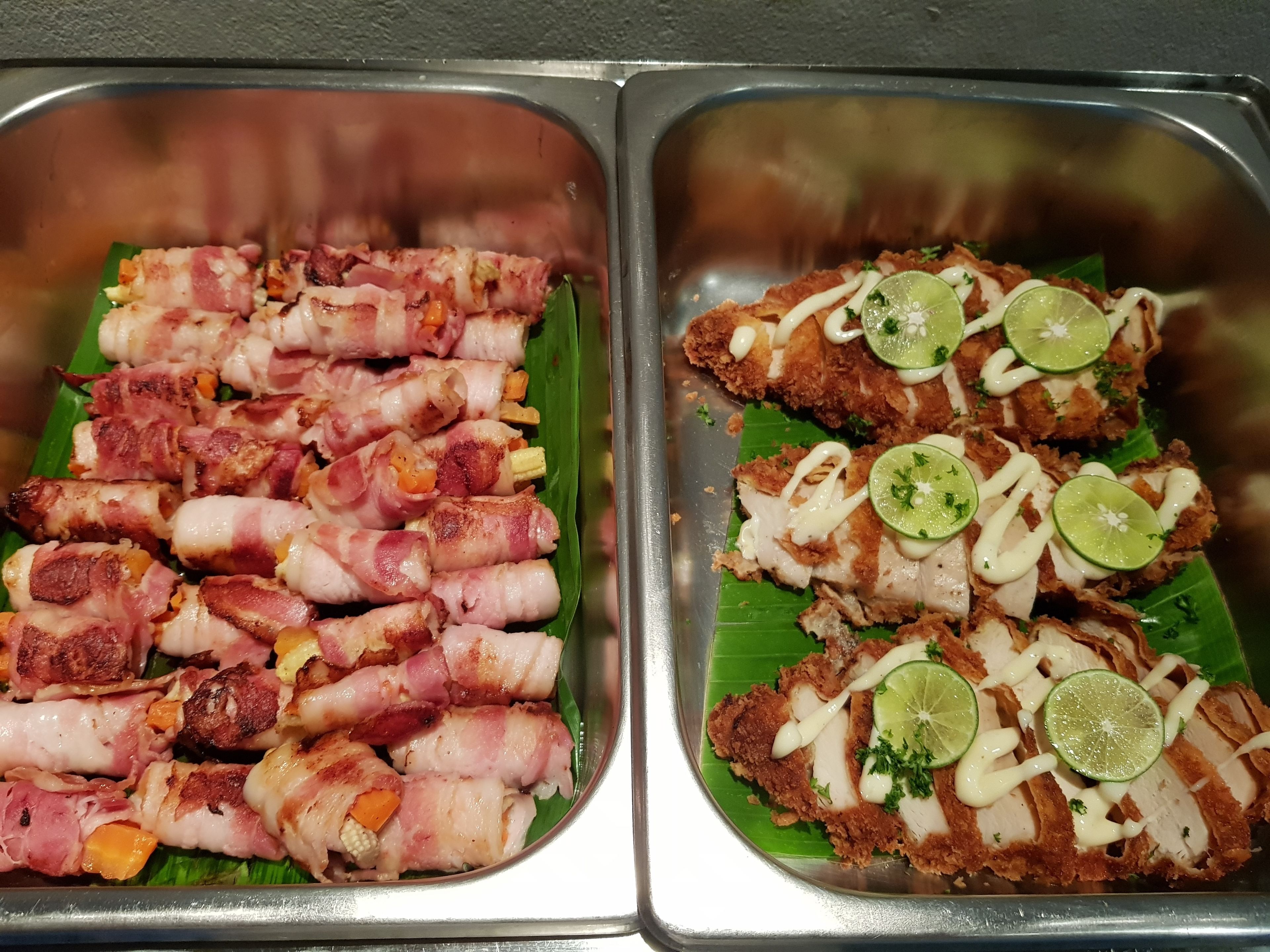Two trays of food, one with bacon-wrapped meatballs and another with fried chicken, both garnished with lime slices and sauce.