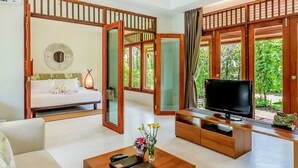 A modern hotel room with a bed, a TV, a coffee table, and a view of greenery through large windows. - L'esprit de Naiyang Beach Resort (Sa Khu)