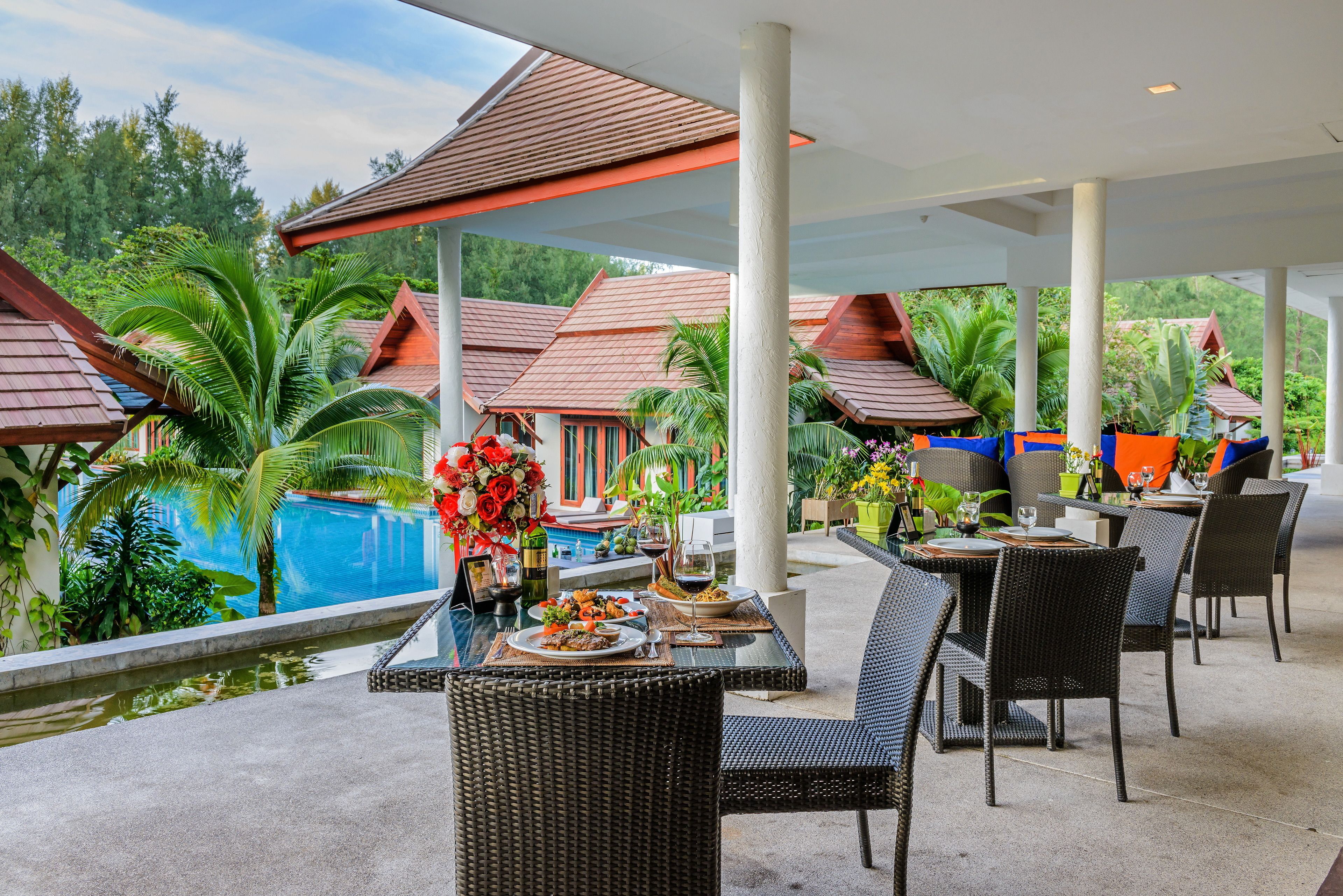 An outdoor dining area with tables and chairs, a pool, and tropical plants.