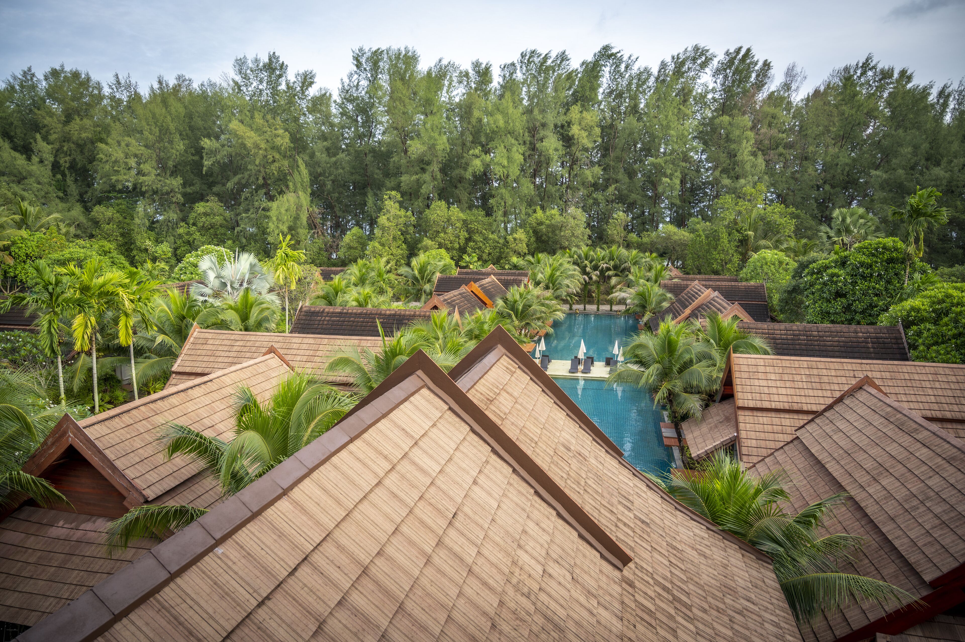 Un resort con varias construcciones tipo bungaló, una piscina central y exuberante vegetación tropical.