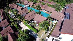 An aerial view of a resort with multiple bungalow-style buildings, a central swimming pool, and lush greenery surrounding the area.