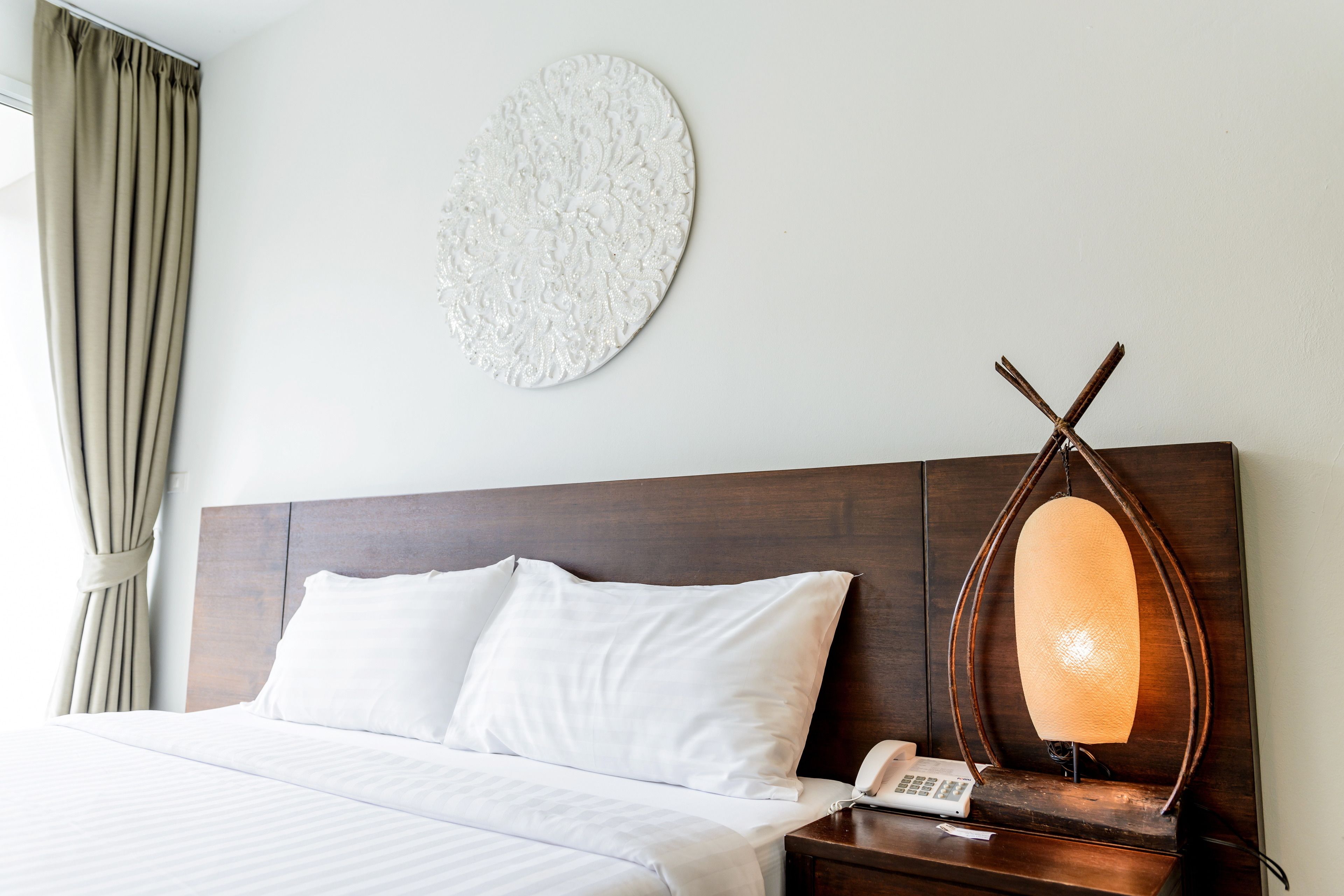 Ein Hotelzimmer mit Bett, Nachttisch mit Lampe, Wanduhr und Vorhang.