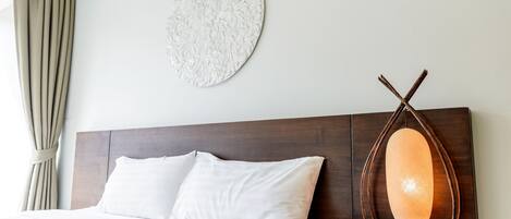A hotel room with a bed, a bedside table with a lamp, a wall clock, and a curtain.