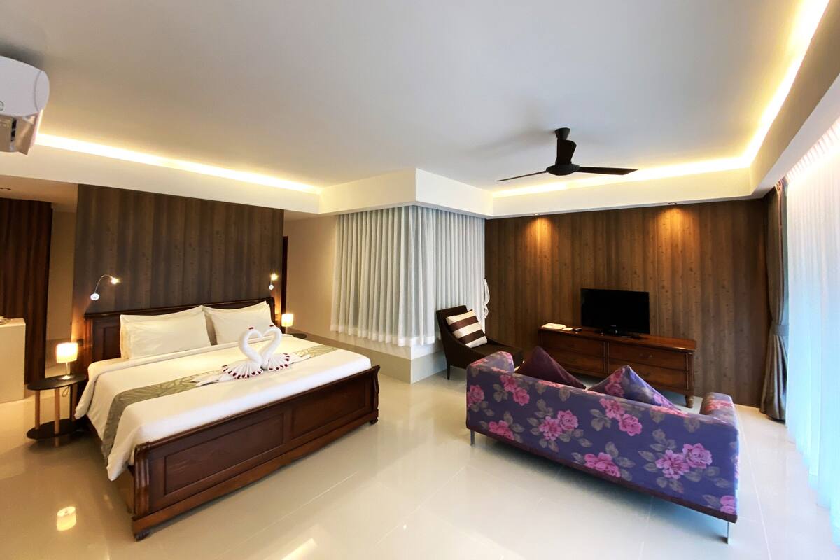 A modern hotel room with a large bed, a sofa, a TV, and a ceiling fan.