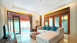 A modern living room with a sofa, a coffee table, and a TV. There is a sliding glass door leading to a pool area. - L'esprit de Naiyang Beach Resort (Sa Khu)