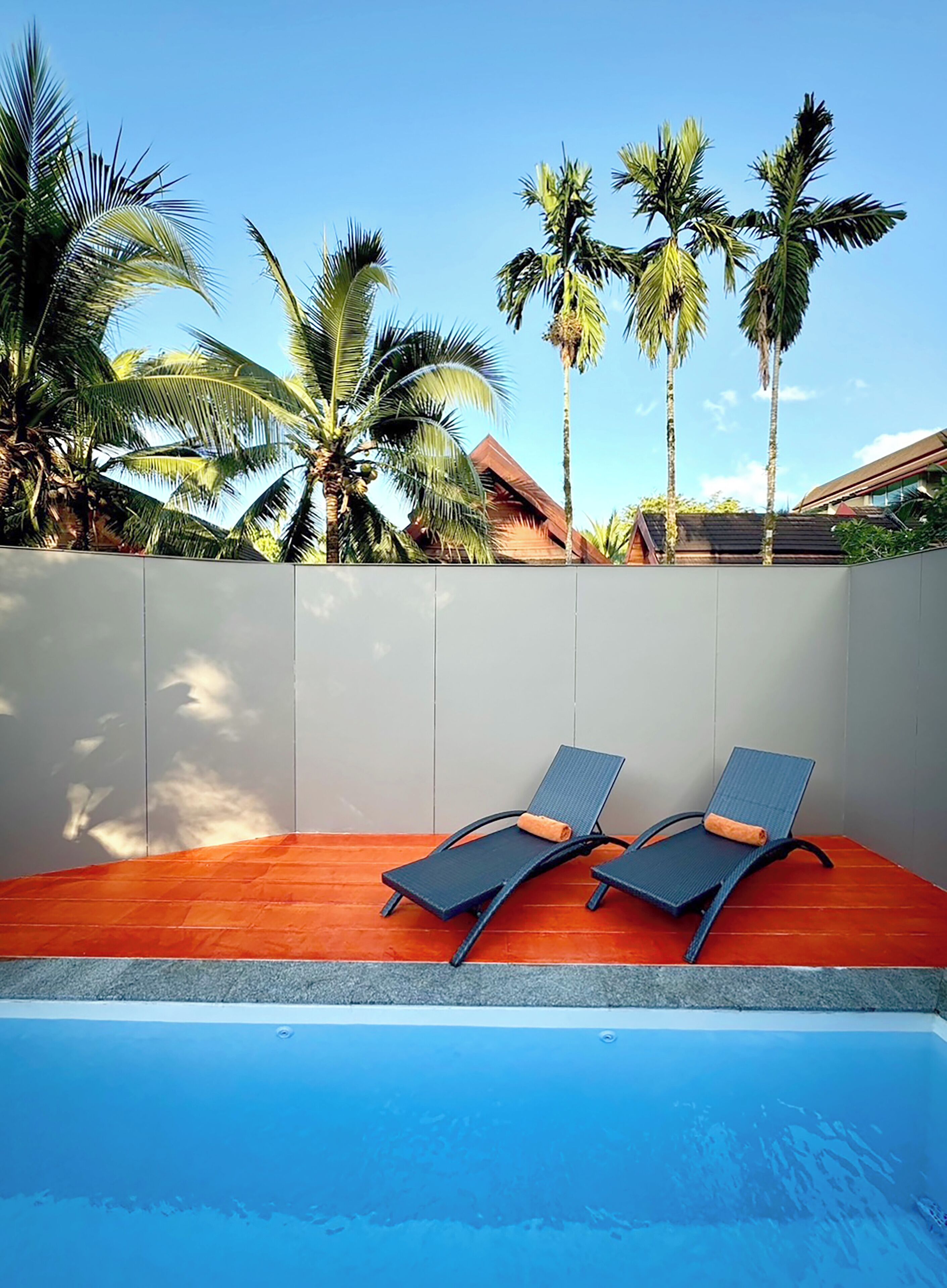 A pool area with two lounge chairs and a white wall.
