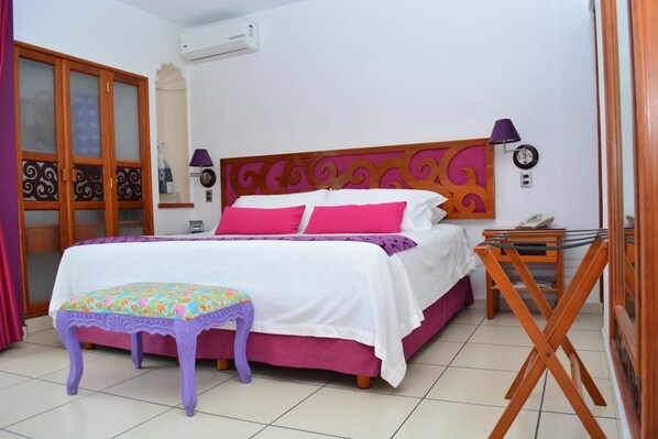 A bedroom with a bed, a small table, a chair, a wardrobe, and a wall-mounted air conditioner.