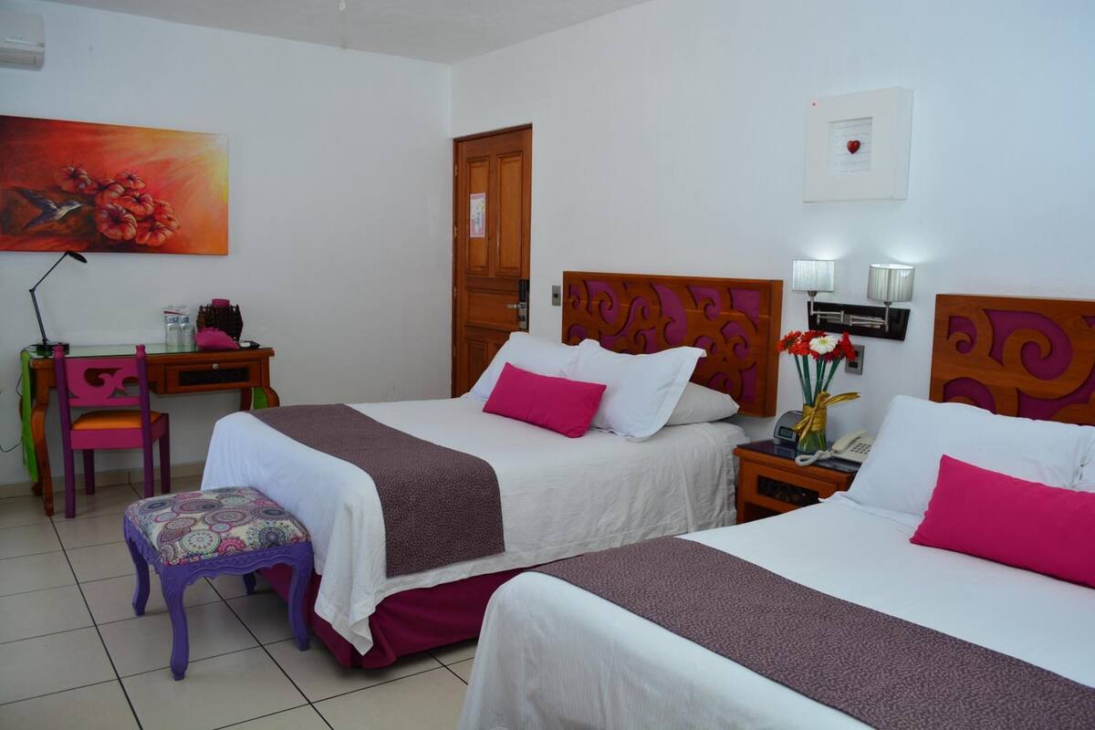 A hotel room with two beds, a desk, a chair, and a painting on the wall.