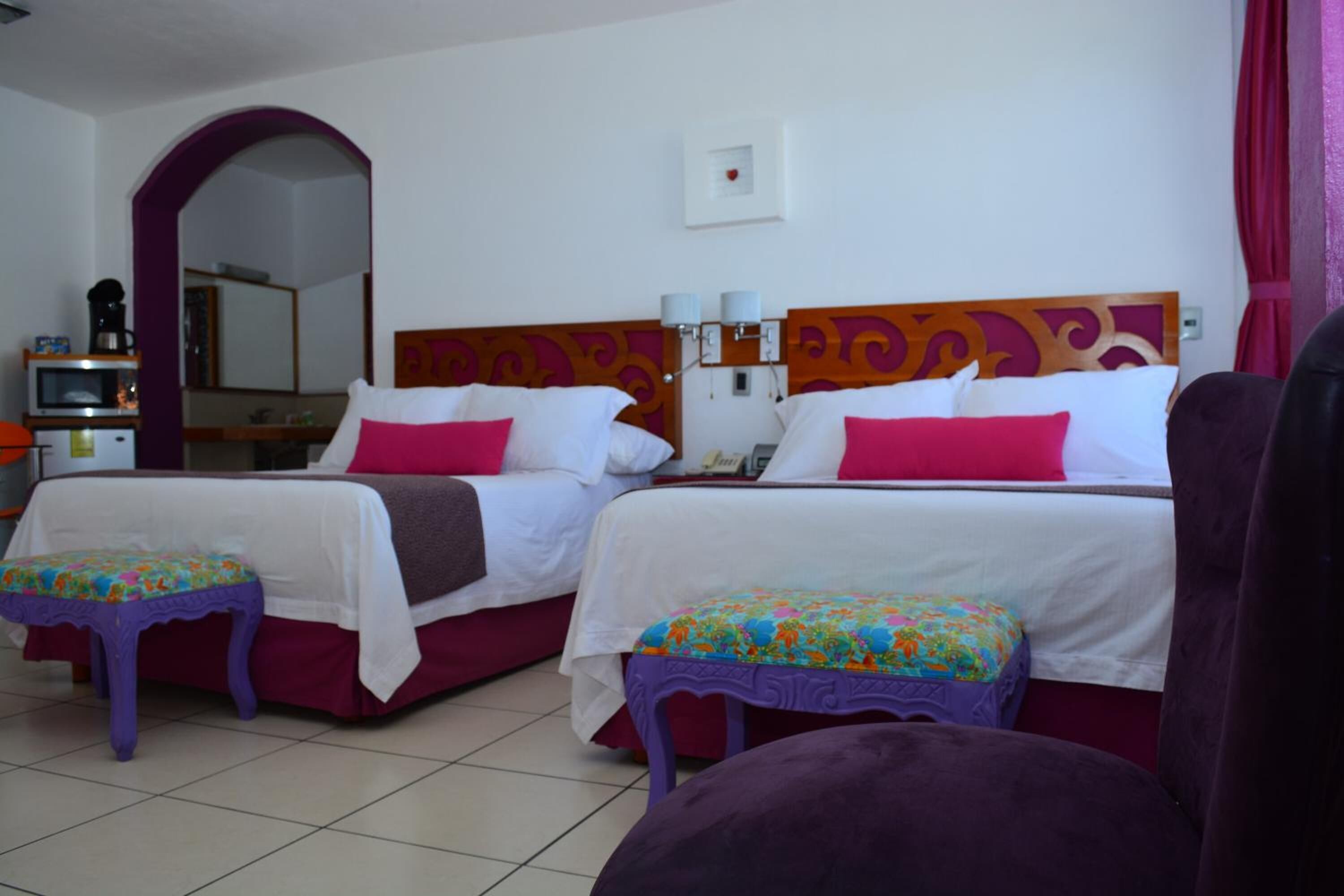 Une chambre d’hôtel avec deux lits, chacun ayant un agencement de couleurs distinct, une petite table, un miroir et une vue sur la salle de bain.