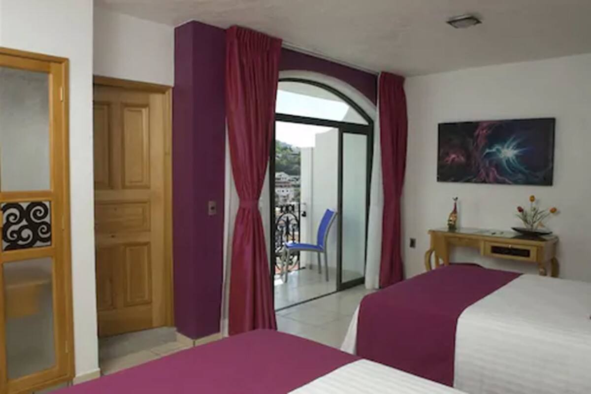 A hotel room with two beds, a desk, a chair, and a view of the outside.