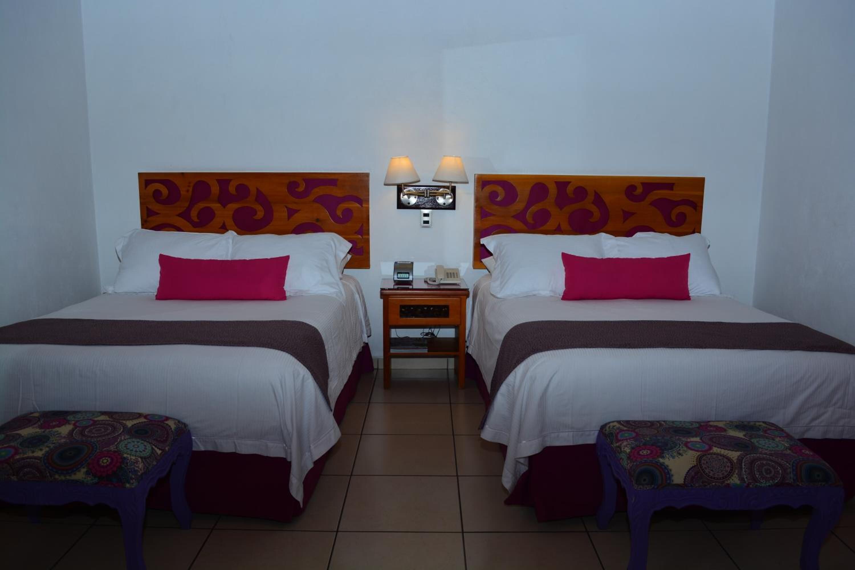 A hotel room with two beds, each with a headboard, a nightstand between them, and a wall-mounted lamp.