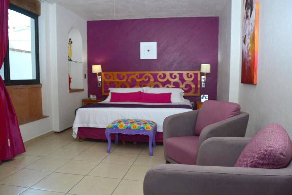 A bedroom with a bed, a chair, a small table, and a window.