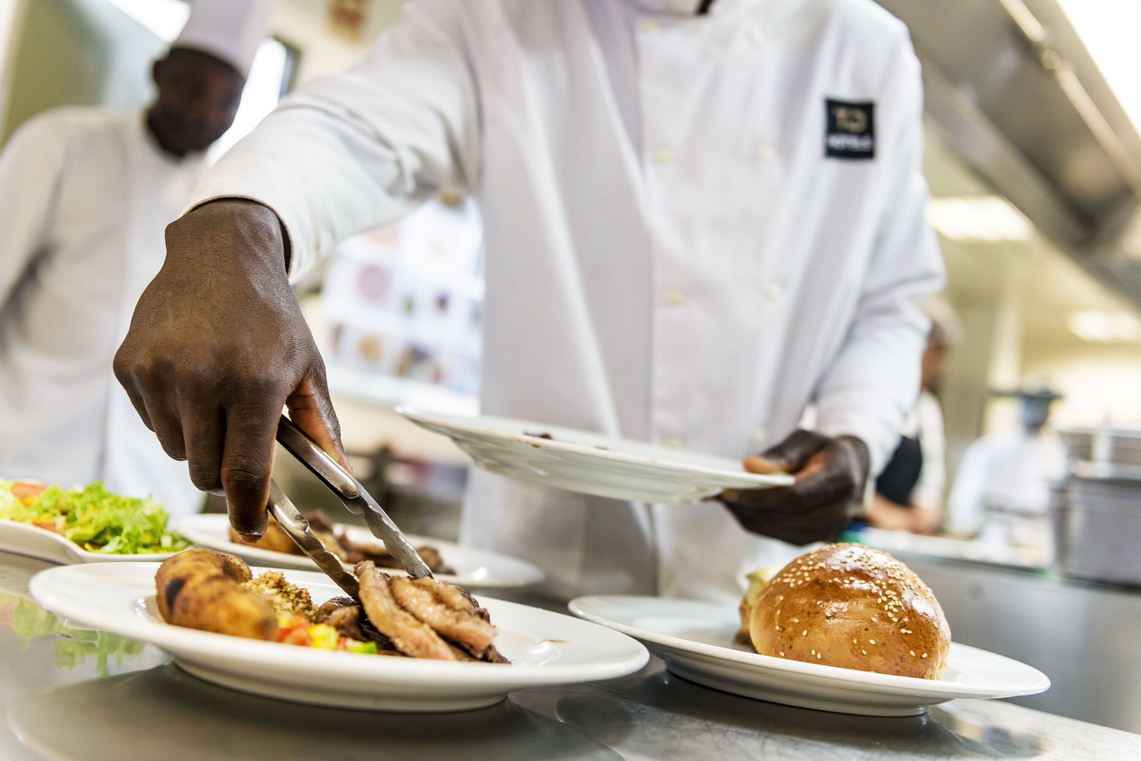 A person serving food in a professional kitchen setting.