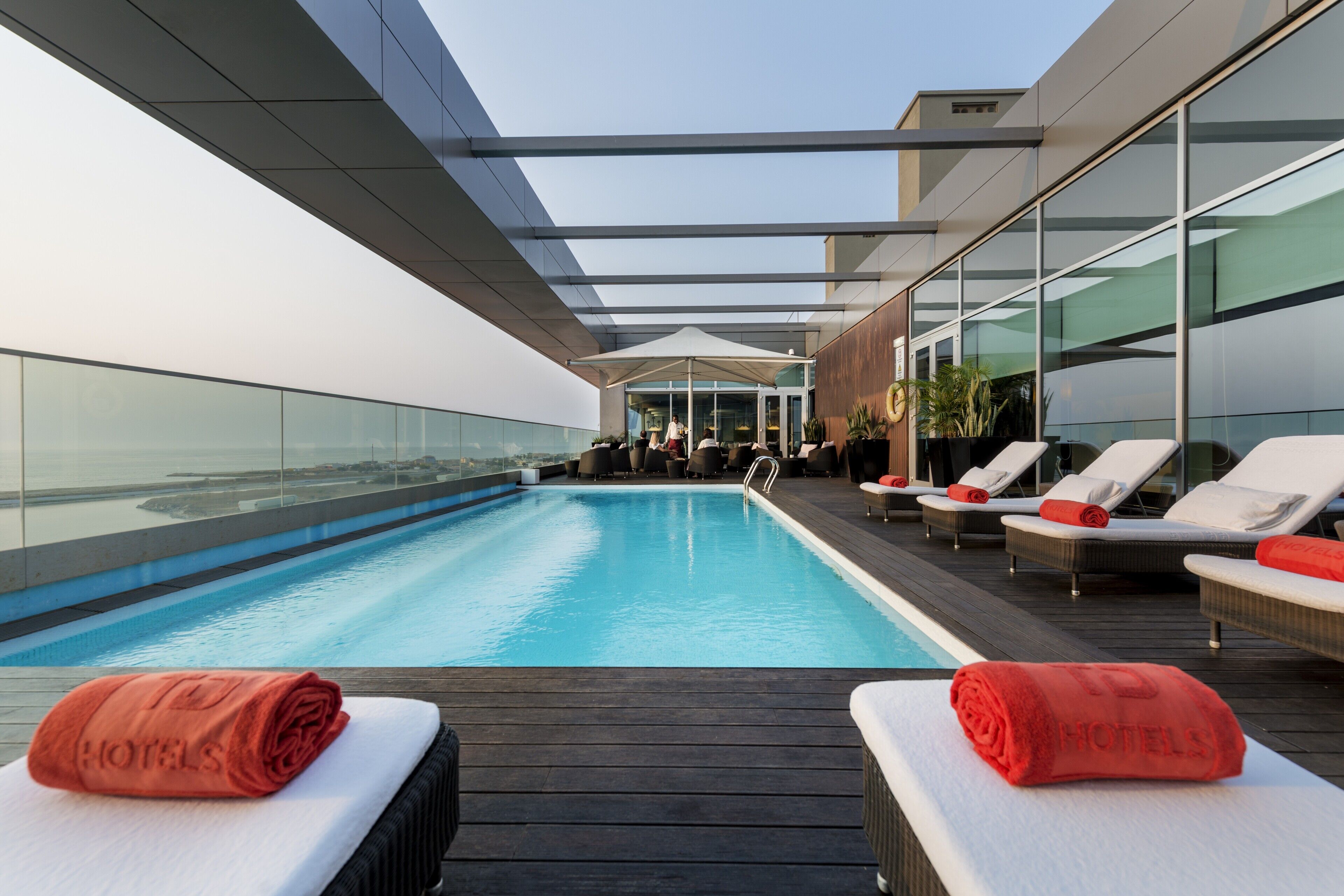 Un espace piscine aménagé sur le toit, avec des chaises longues et une balustrade en verre.